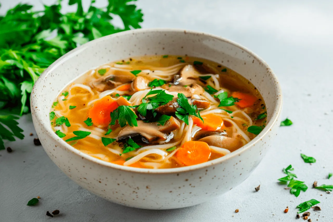 Aksamitny rosół z makaronem, pieczarkami i marchewką. Idealne jakie przyprawy do rosołu, by podkreślić smak? Świeża natka pietruszki i ziarna pieprzu.