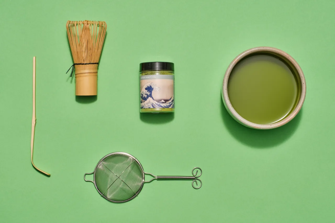 Akcesoria do przygotowania matcha: bambusowa miotełka (chasen), bambusowa łyżeczka (chashaku), sitko, słoiczek z matchą i gotowy napój w miseczce. Idealne do nauki, jak pić matcha.