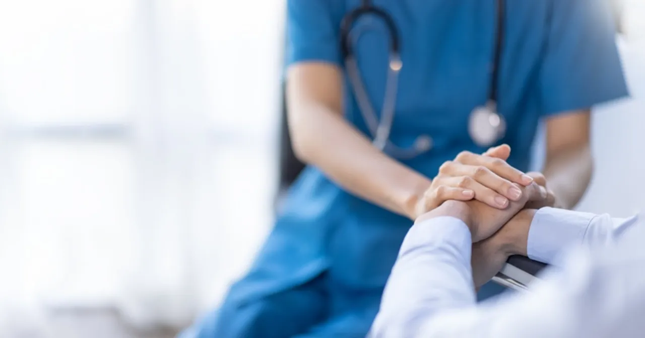 Dłoń pielęgniarki w niebieskim uniformie wspiera dłoń pacjenta. To symboliczne zakończenie leczenia i nadzieja na lepsze jutro.