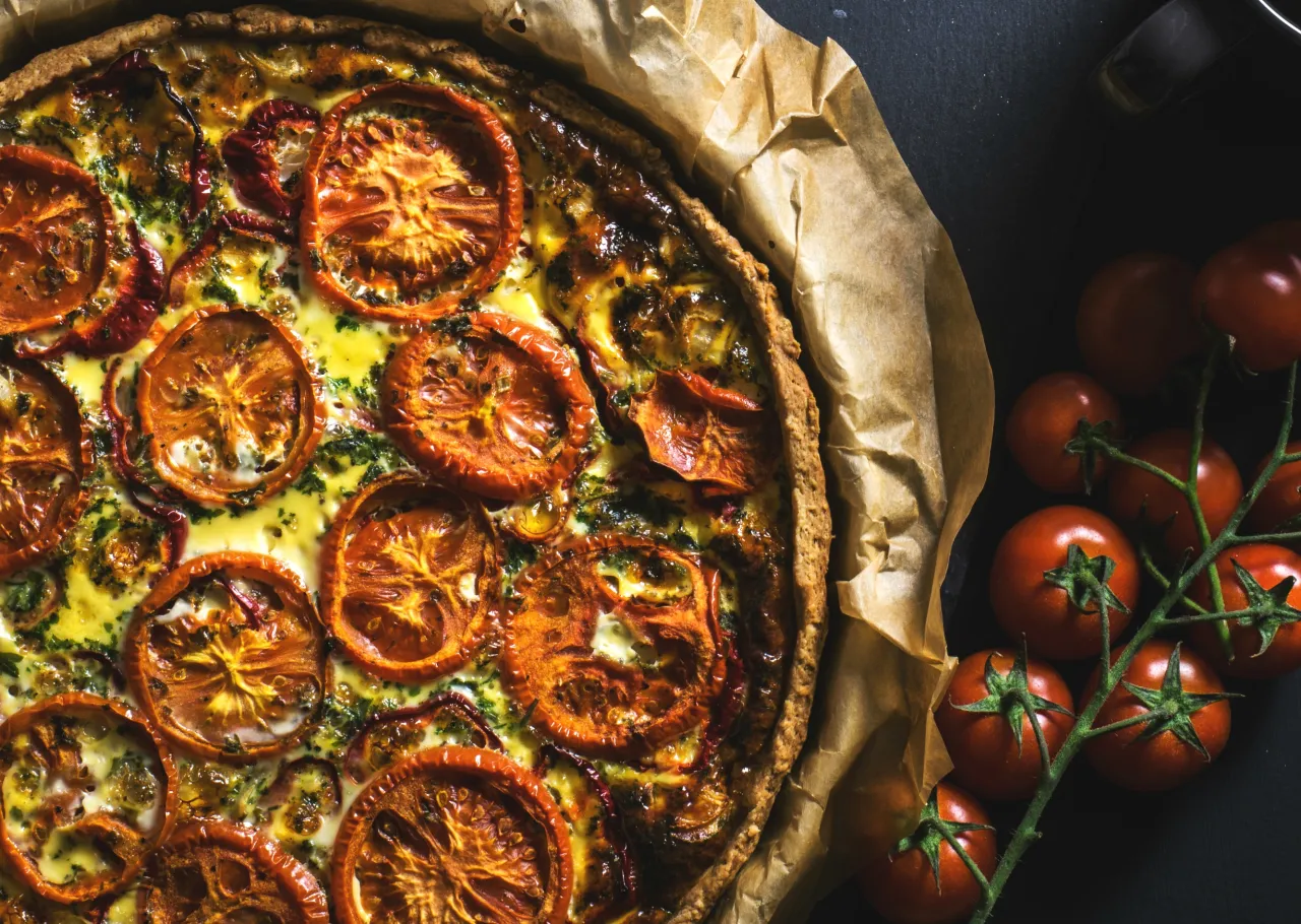 Pyszne ciasto na tartę wytrawną z pomidorami i ziołami, pieczone na papierze, obok świeże pomidorki.