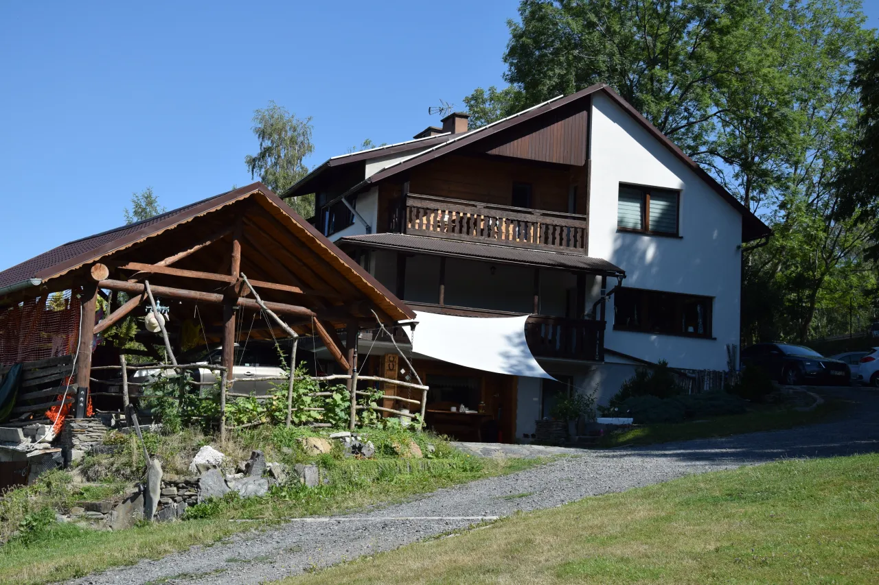 Agroturystyka bac&oacute;wka Giemzik&oacute;w to urokliwe miejsce z drewnianą wiatą i domem z balkonem, otoczone zielenią.