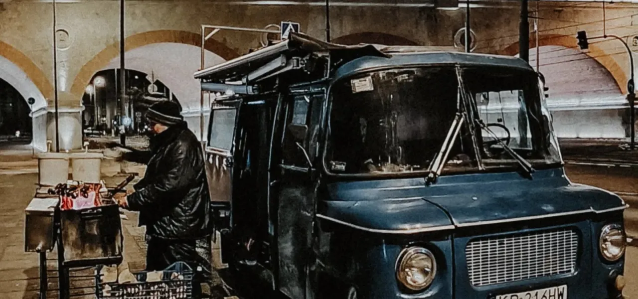 Sprzedawca przygotowuje kiełbaski z niebieskiej Nyski, stojącej pod łukami.