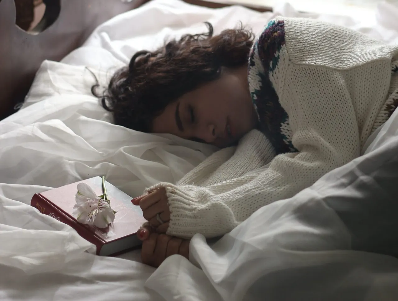 Kobieta śpi na łóżku obok książki z kwiatem. Czy można się modlić na leżąco?