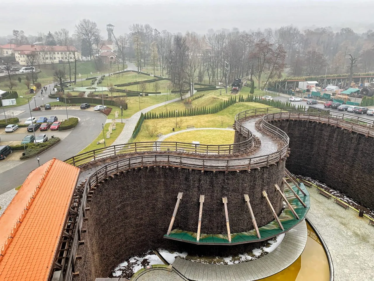 Drewniana tężnia solankowa i park to atrakcje, co można zwiedzić w Wieliczce. W tle budynki i wieża.