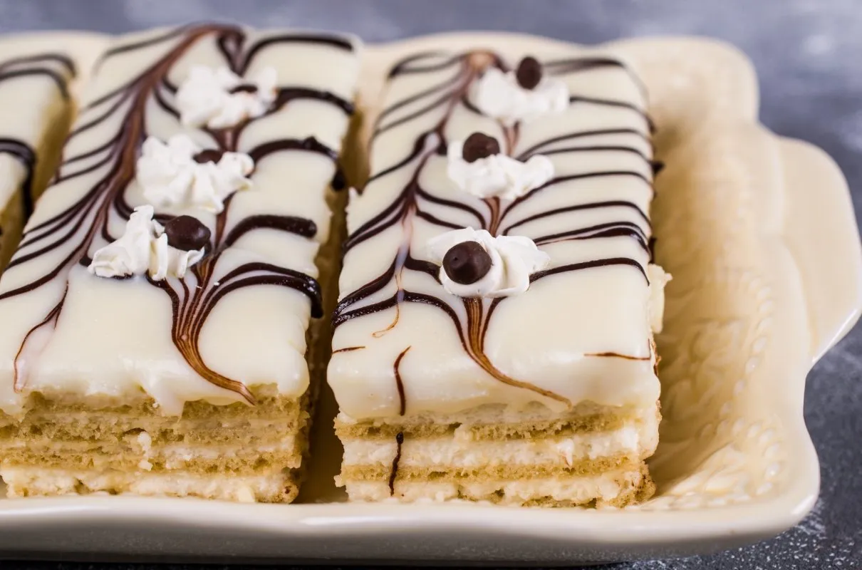 Słodkie ciasto z herbatnikami, oblane białą czekoladą z czekoladowymi wzorami i bitą śmietaną. Idealne na deser, gdy szukasz inspiracji na przepisy na ciasto z herbatnikami.