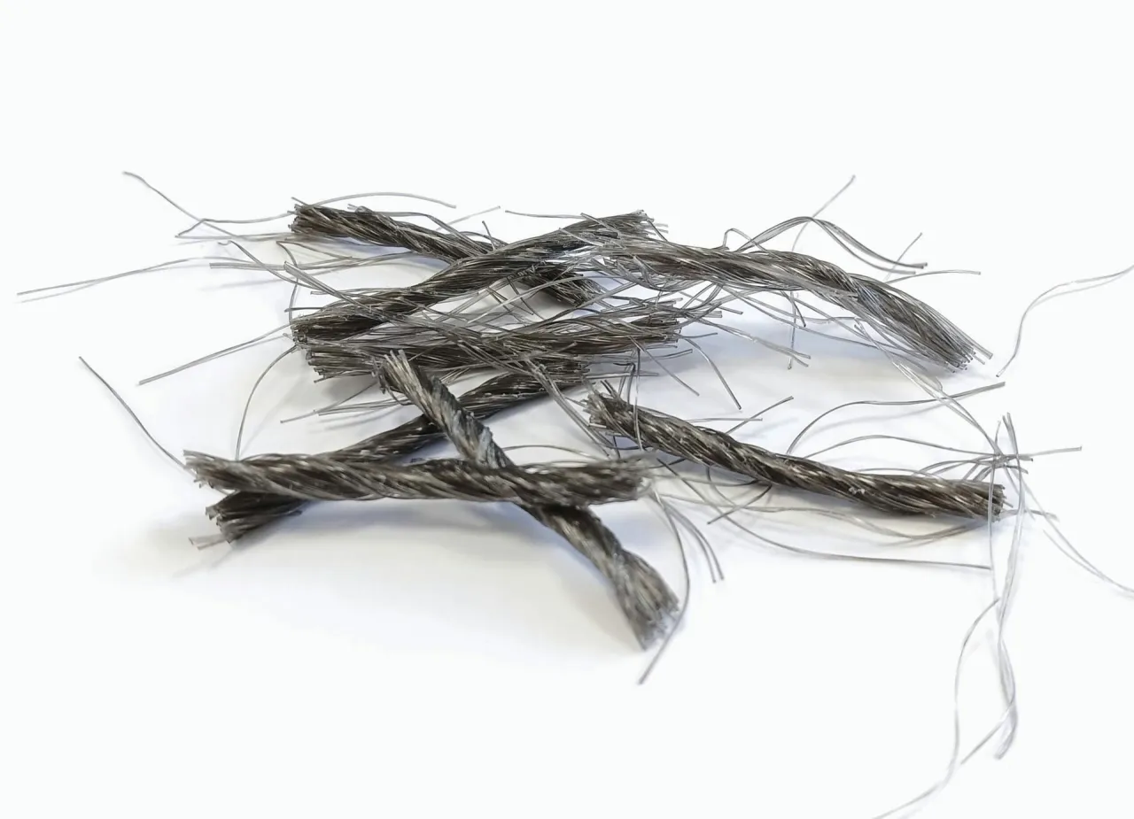 Splecione, metaliczne włókna do betonu, tworzące chaotyczną plątaninę na białym tle.