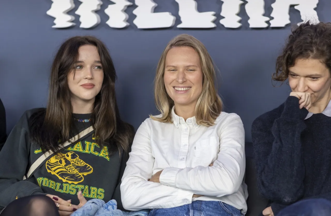 Trzy kobiety siedzą obok siebie. Jedna z nich, w czarnej bluzie z napisem 