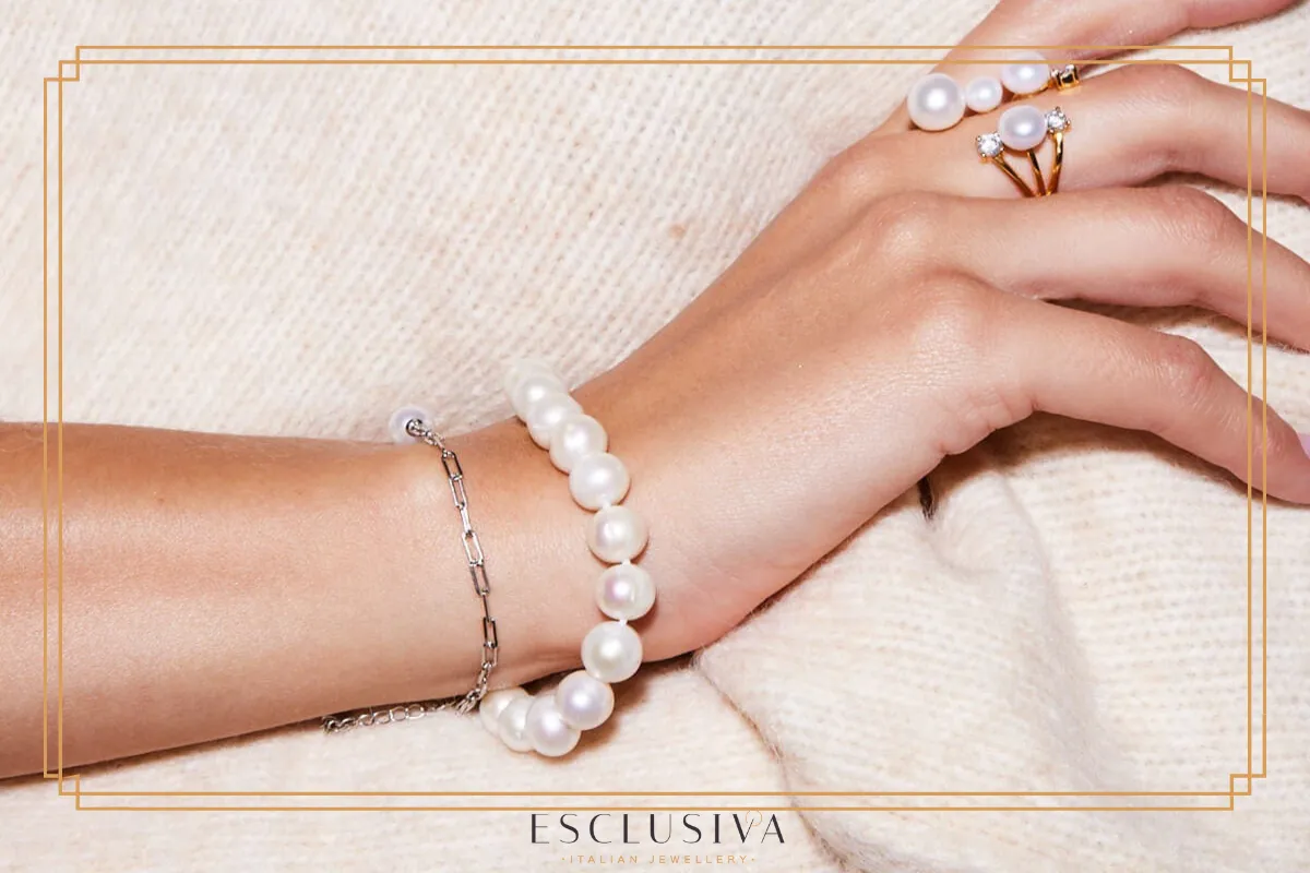 Dłoń ozdobiona bransoletką z pereł i pierścionkiem z brylantami. Jak rozpoznać prawdziwe perły? Ich blask i gładkość to klucz.
