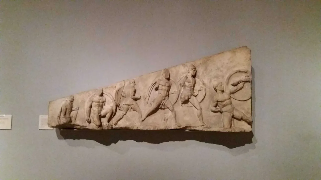 Kamienna płaskorzeźba przedstawia grupę wojowników w ruchu, być może scenę bitwy. To dzieło nawiązuje do stylu Fidiasza, ukazując dynamikę i siłę.