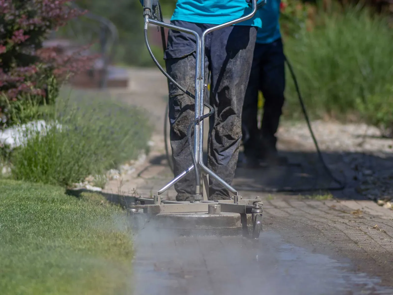 Osoba czyści ścieżkę z kamyczk&oacute;w w ogrodzie za pomocą myjki ciśnieniowej.