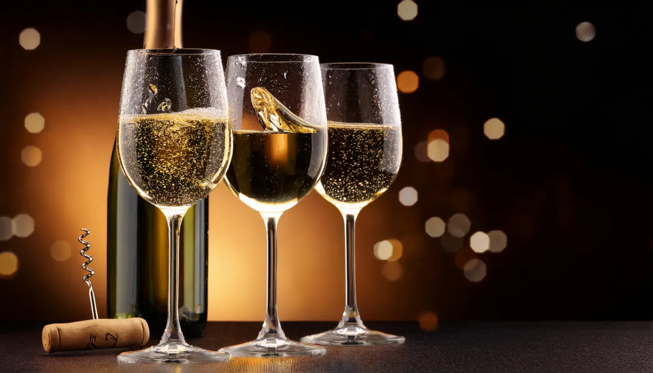 Trzy kieliszki musującego prosecco drink, butelka i korkociąg na tle rozmytych świateł.