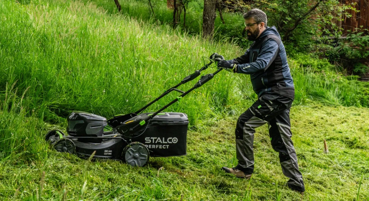 Mężczyzna z kosiarką Stalco Perfect w wysokiej trawie. Odpowiedź na pytanie, jak często kosić trawę, zależy od jej wzrostu.