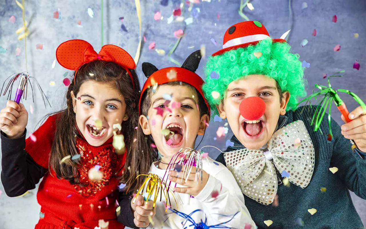 Trójka roześmianych dzieci w karnawałowych strojach, z konfetti i serpentynami. Idealny pomysł, jak ubrać dziecko na bal karnawałowy!