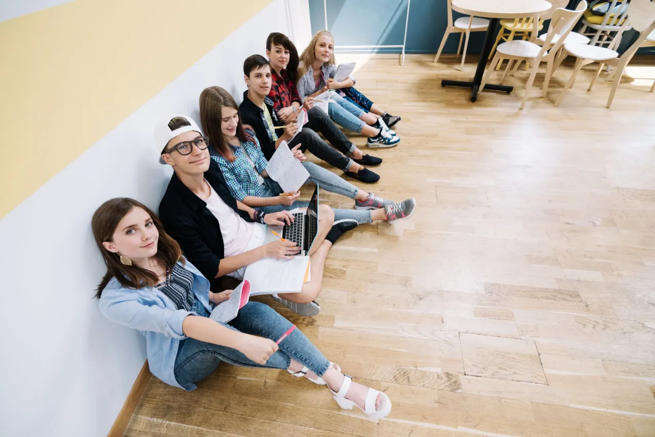 Grupa uczniów siedzi na podłodze, ucząc się. Zastanawiają się, ile lat trwa liceum.
