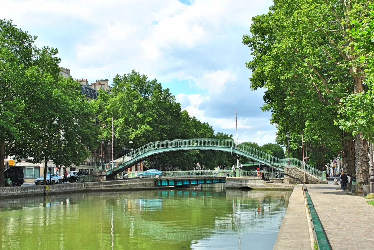 Zielony mostek nad kanałem w 10 dzielnicy Paryża, otoczony drzewami.