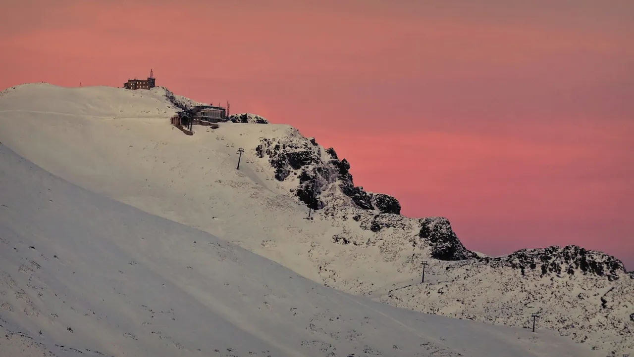 Zach&oacute;d słońca nad Kasprowym Wierchem. Czy szlak na Kasprowy Wierch jest trudny? Widok na ośnieżone szczyty i wyciągi narciarskie.