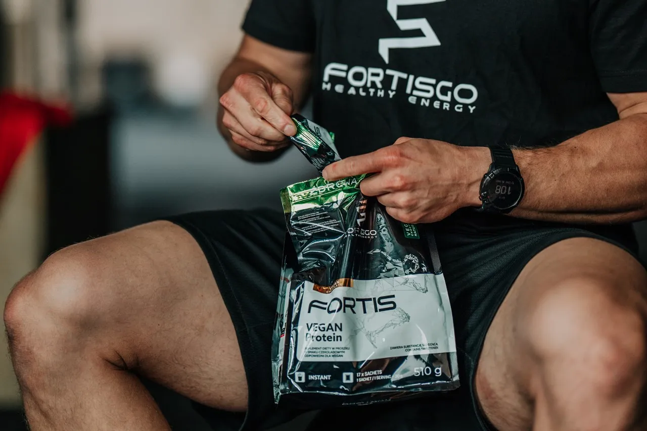 Mężczyzna otwiera opakowanie wegańskiego proteinowego shake'a. Czy shake proteinowy jest zdrowy? To zależy od składu i celu.