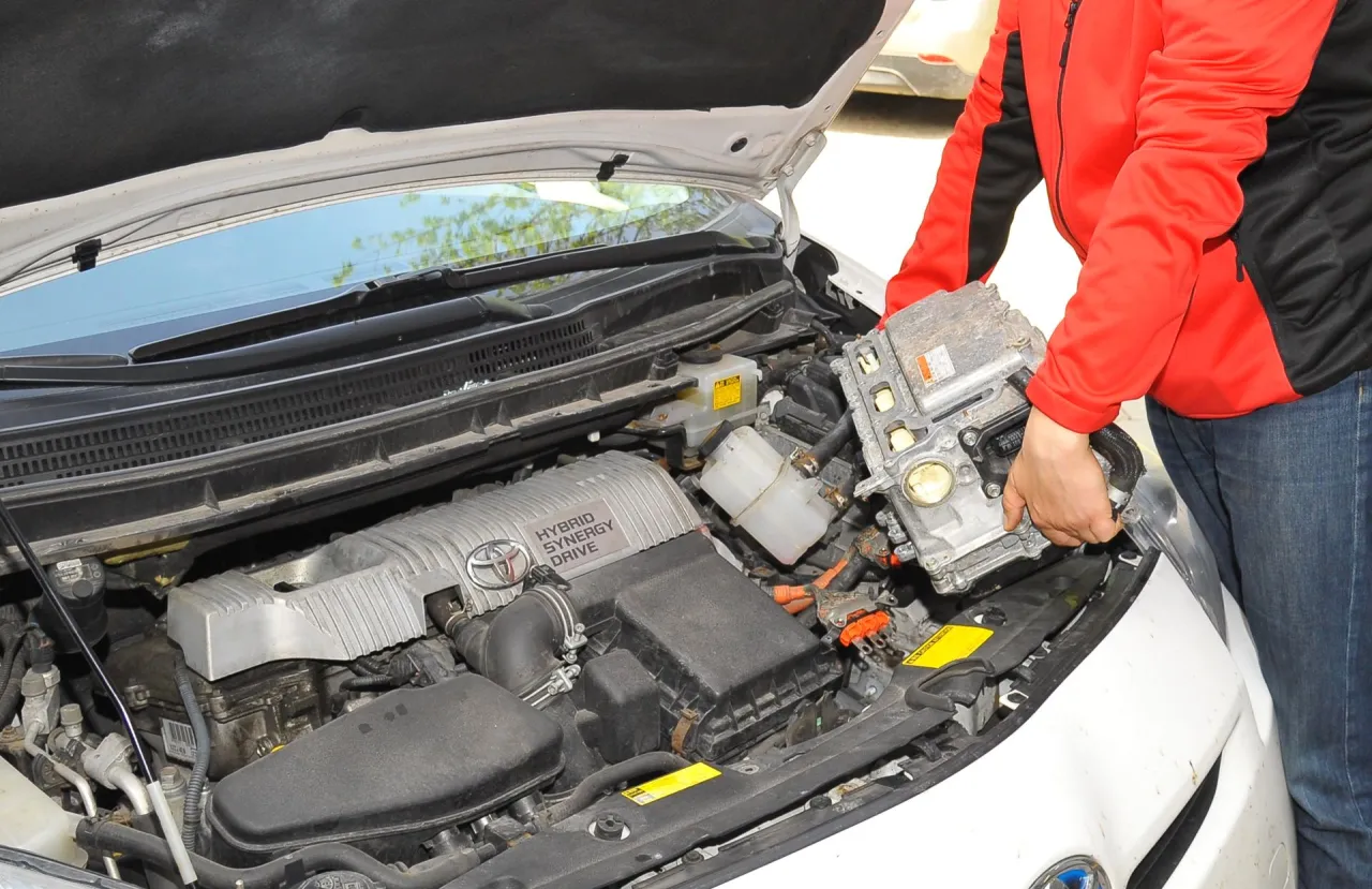 Osoba wyjmuje moduł sterujący z silnika Toyoty Yaris Hybrid. To nie jest akumulator, ale ważny element układu hybrydowego.