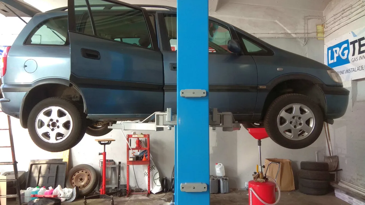 Samochód na podnośniku w warsztacie. Czekamy na szybką odpowiedź, ile trwa wymiana oleju.