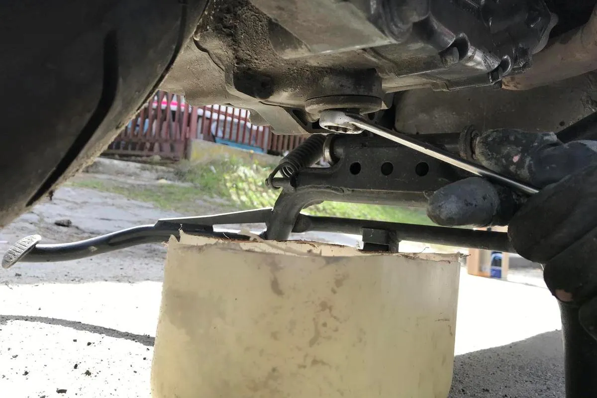 Wymiana oleju w motocyklu. Klucz odkręca korek spustowy, a pod spodem stoi pojemnik na zużyty olej.