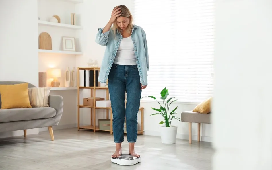 Kobieta w średnim wieku mierząca się z wagą, zmartwiona, ale z nadzieją