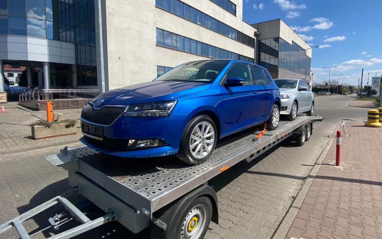 Niebieska Skoda na lawecie, obok srebrny samochód. Zastanawiasz się, ile kosztuje laweta?