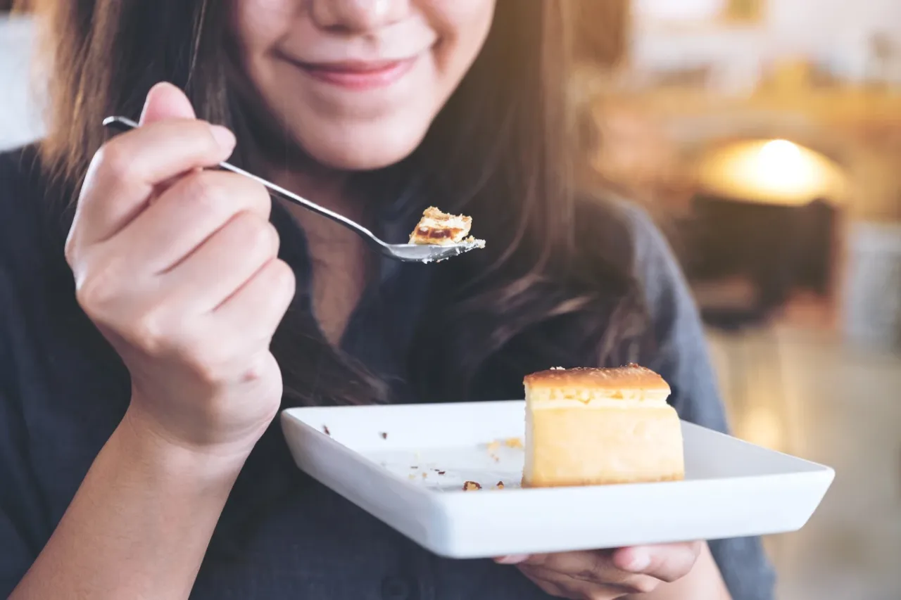 Uśmiechnięta kobieta je deser z widelca. Czy desery lepiej jeść przed głównym posiłkiem?