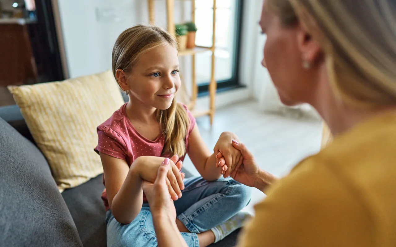 Dziewczynka i dorosły rozmawiają, trzymając się za ręce. To ważny moment, jak rozmawiać z dzieckiem o samobójstwie rodzica, budując zaufanie.