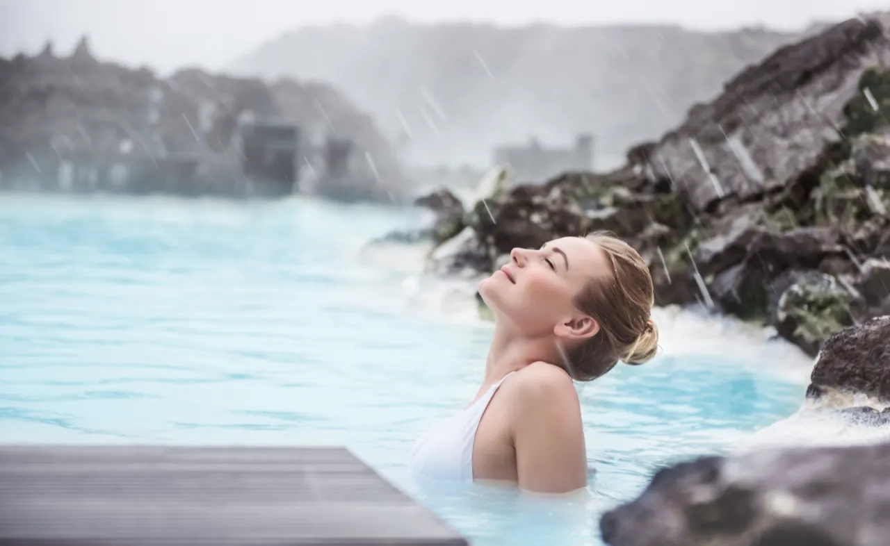 Kobieta relaksuje się w Blue Lagoon, basenie geotermalnym, podczas deszczu.