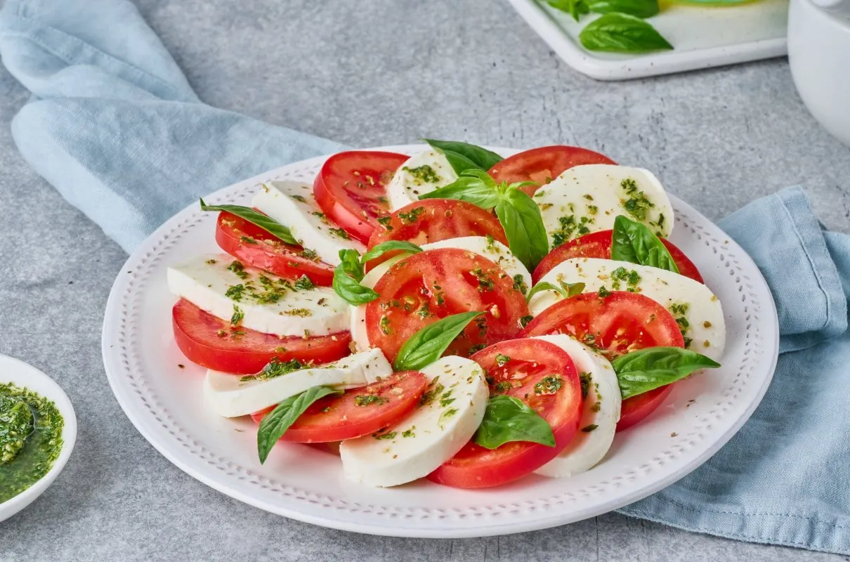 Sałatka Caprese z pomidor&oacute;w i mozzarelli, posypana ziołami. Bazylia do czego dodawać? Do tej pysznej sałatki!