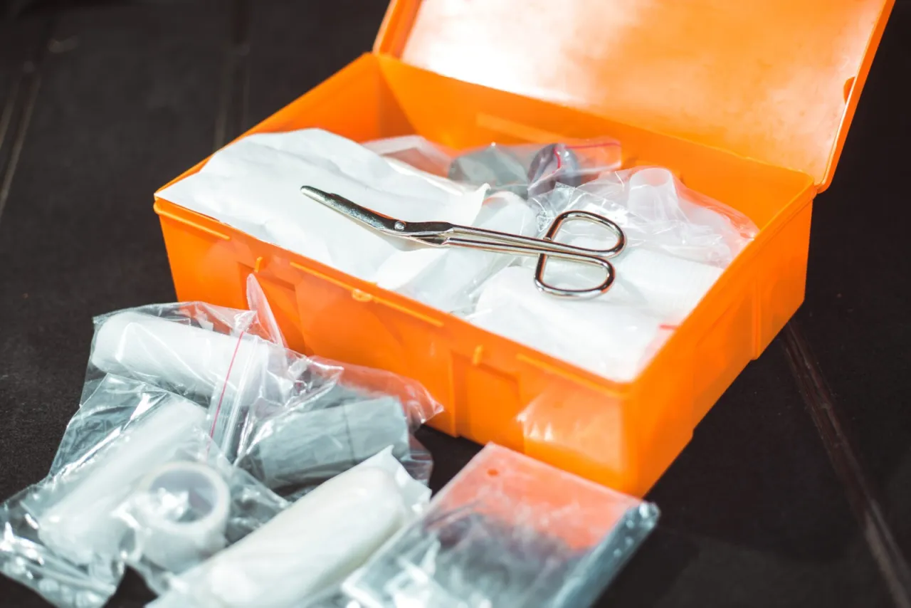 Pomarańczowa apteczka samochodowa z wyposażeniem: nożyczki, bandaże, plastry. Gotowa na nieprzewidziane sytuacje.