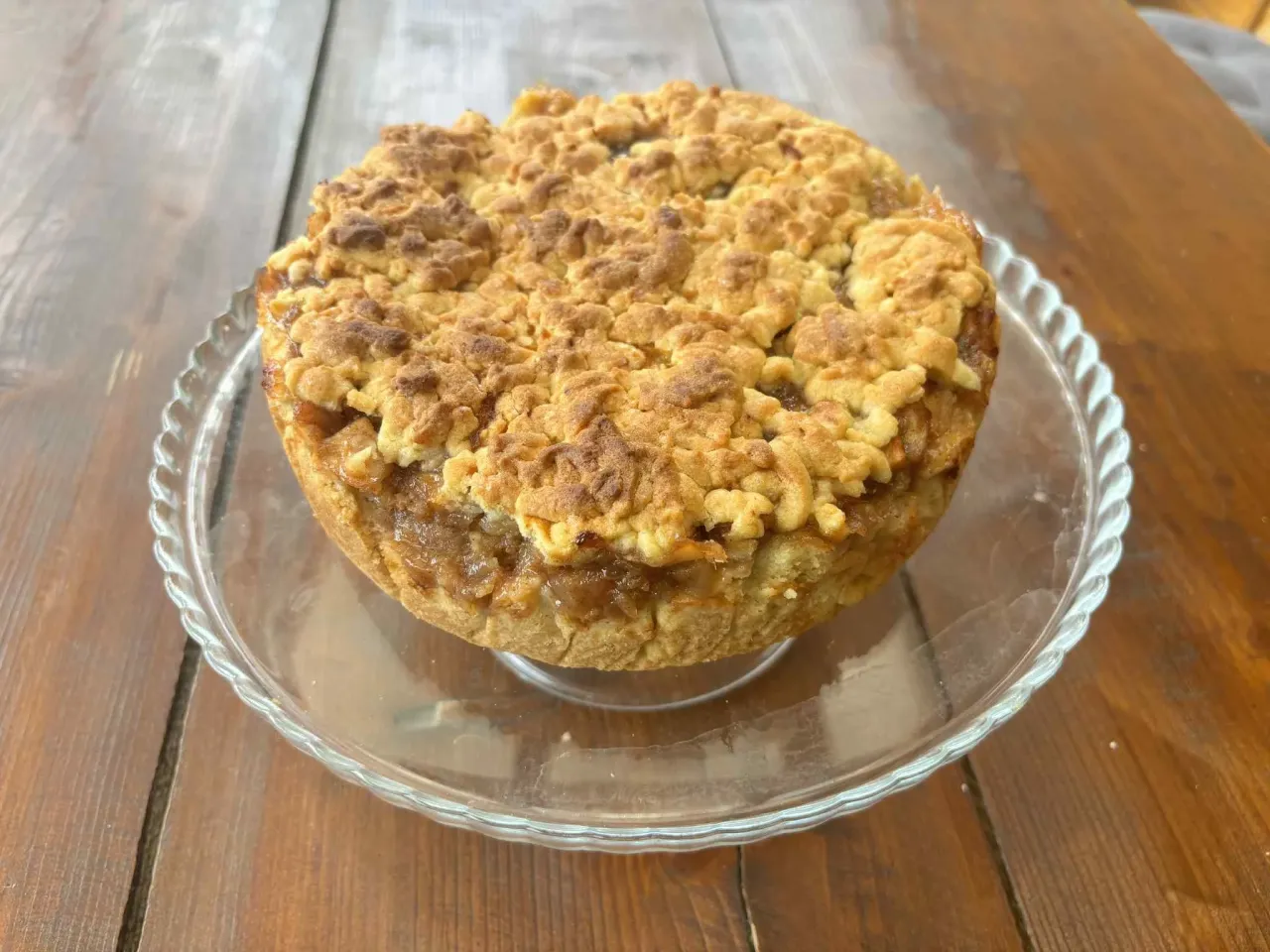 Pyszna szarlotka z kruszonką na szklanej paterze. Idealna na podwieczorek, a jej prosty przepis zachwyci każdego.