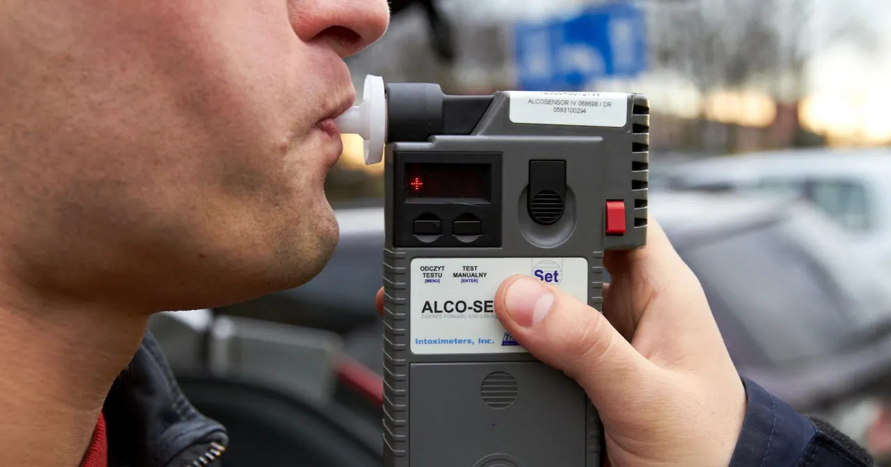 Mężczyzna dmucha w alkomat, urządzenie, gdzie można zbadać się alkomatem. Wynik testu na trzeźwość jest wyświetlany na ekranie.