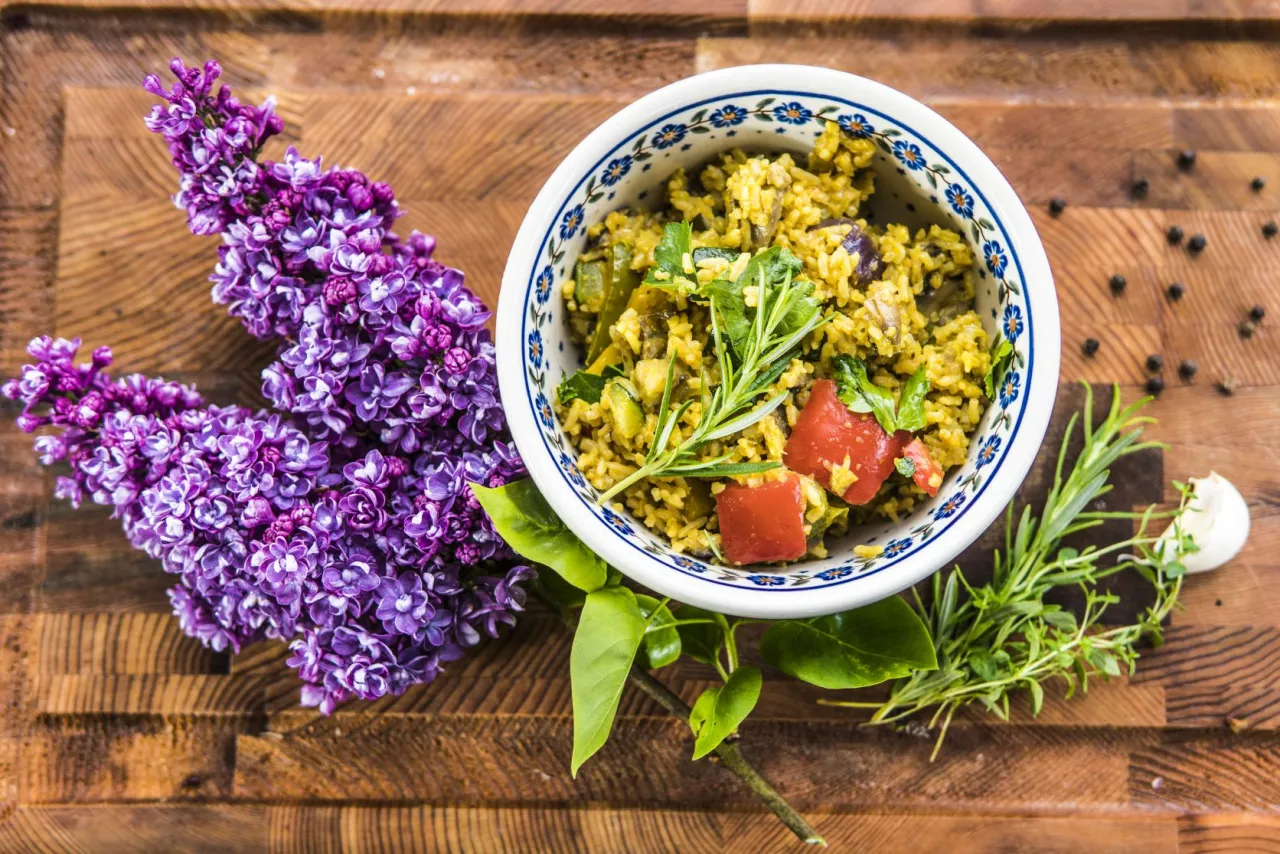 Aromatic tajskie curry z warzywami w misce, ozdobione rozmarynem i pomidorami, obok bukietu bzu na drewnianej desce.