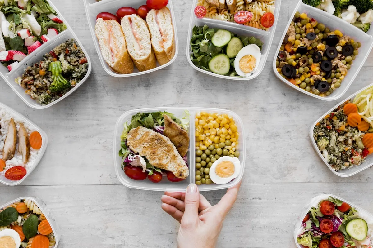 Jakie są opcje menu w cateringu imprezowym? Różnorodne dania w pojemnikach: sałatki, kanapki, kurczak z warzywami, makaron, ryż.