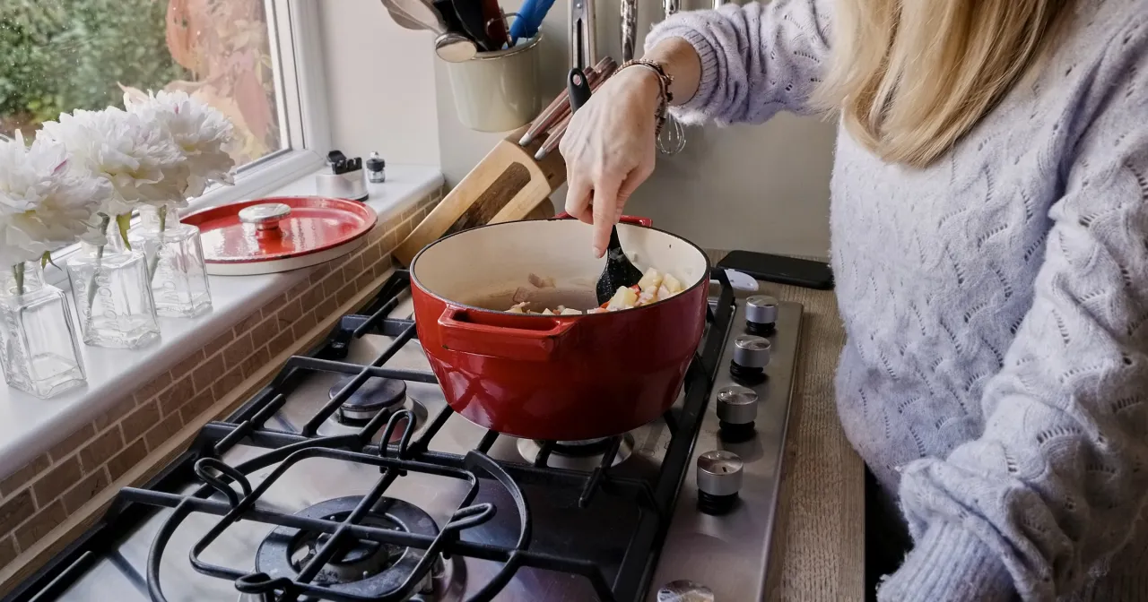Kobieta miesza składniki w czerwonym garnku na kuchence, ucząc się, jak gotować zdrowo i dietetycznie.
