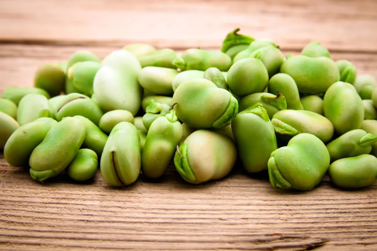 Kupa świeżego bobu na drewnianym tle. Zastanawiasz się, ile kalorii ma b&oacute;b? Jest niskokaloryczny i pełen białka.