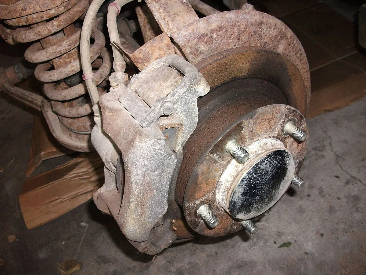 Zardzewiały zacisk hamulcowy i tarcza, gotowe do regeneracji zacisk&oacute;w hamulcowych. Widoczna sprężyna zawieszenia.