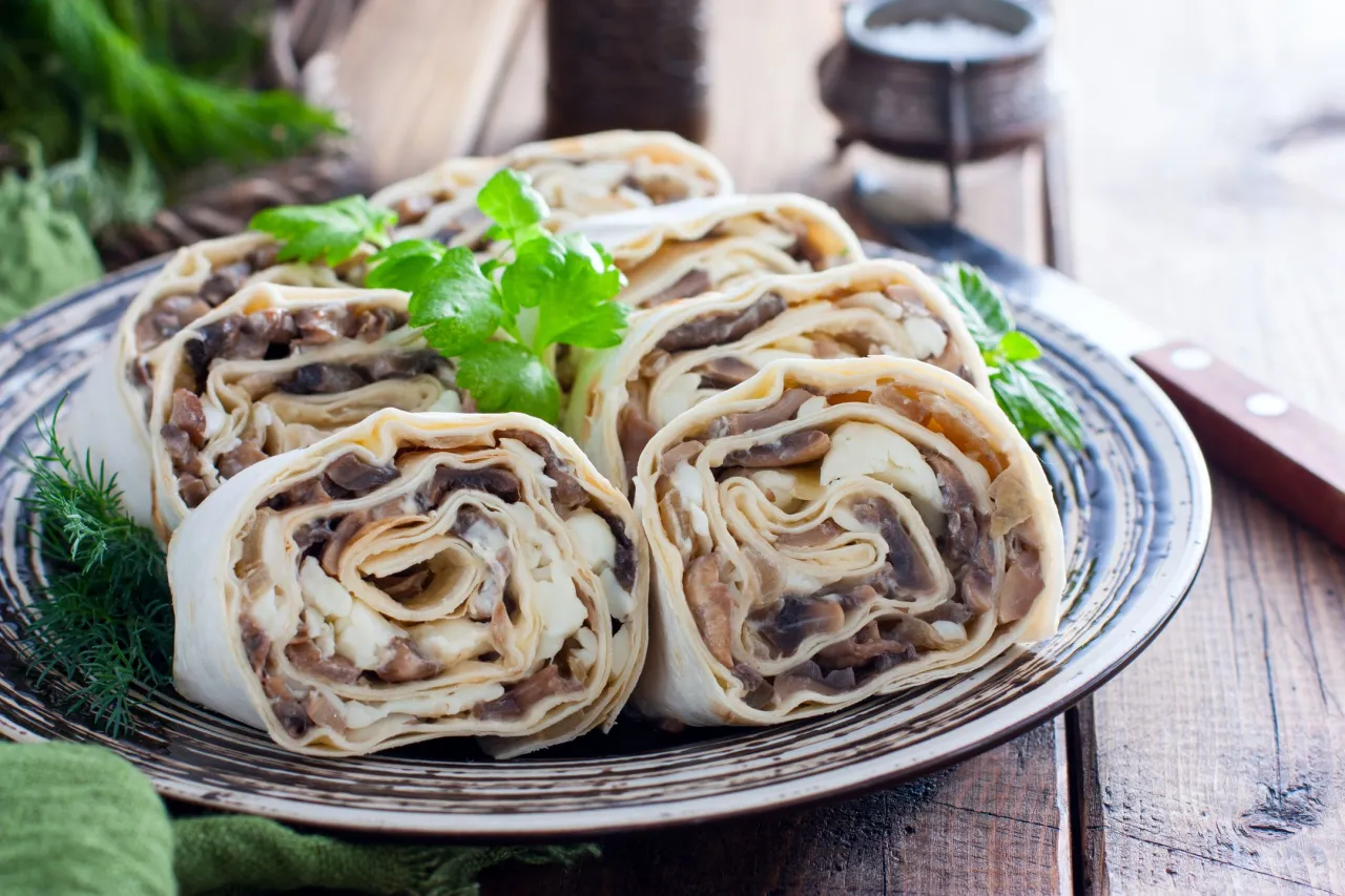 Roladki z lawaszu z grzybami i serem, pięknie ułożone na talerzu, ozdobione natką pietruszki.