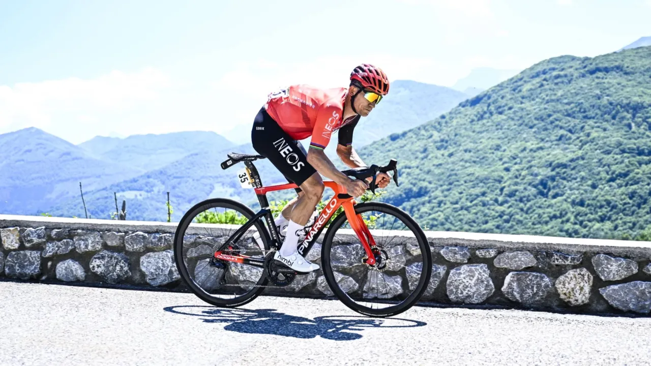 Michał Kwiatkowski, kolarz Ineos Grenadiers, w czerwonej koszulce i kasku, ściga się na g&oacute;rskiej trasie.