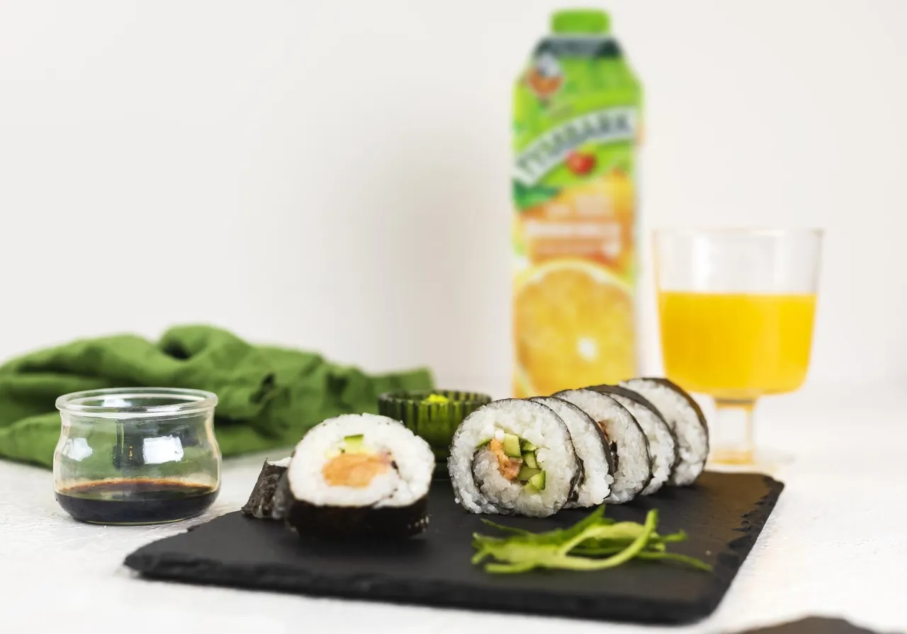 Pyszne sushi z łososiem, og&oacute;rkiem i ryżem, podane z sosem sojowym i sokiem pomarańczowym.