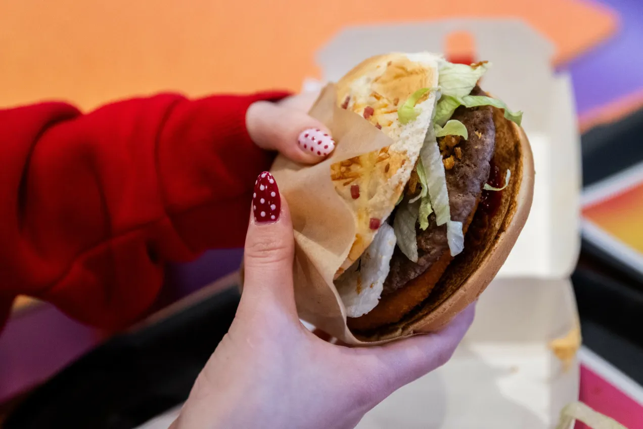 Ręka w czerwonym swetrze trzyma burgera. To idealna przekąska, gdy kończy się sezon na drwala i czas na coś pysznego.