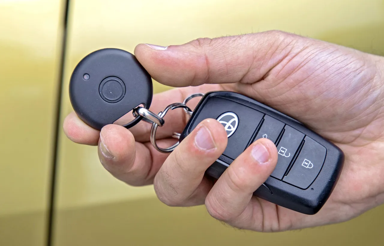 Dłoń trzyma kluczyki samochodowe i okrągły brelok. To część systemu, jak zabezpieczyć samoch&oacute;d przed kradzieżą.