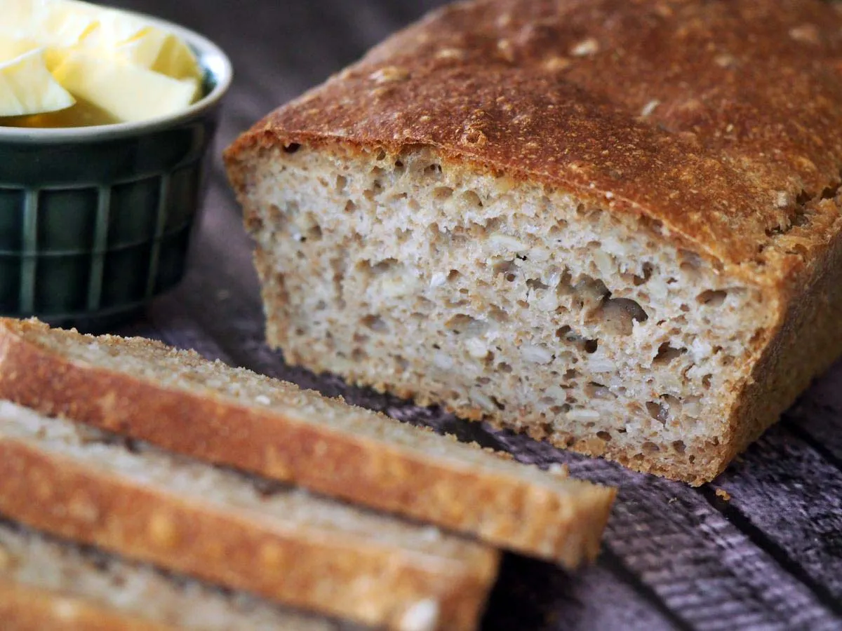 Chleb pełnoziarnisty, idealny do nauki, jak upiec chleb dietetyczny. Kromki i masło w miseczce.