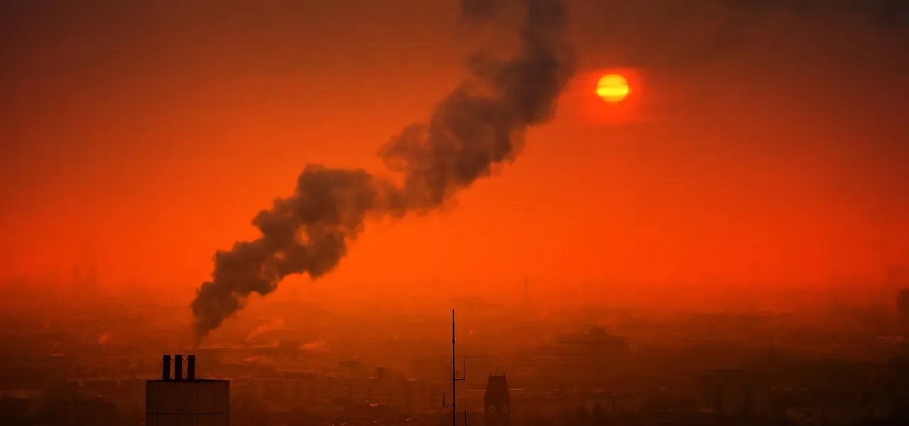 Zachód słońca nad miastem, gdzie ciemny dym z komina tworzy widok, który odpowiada na pytanie: co to smog.