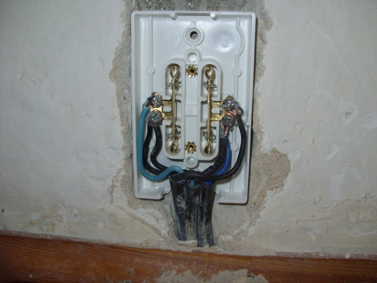 Widok wnętrza puszki elektrycznej z podłączonymi przewodami. Widoczne są zaciski śrubowe i przewody: niebieski, czarny i brązowy. Może to być przyczyna małego napięcia na przewodzie neutralnym.