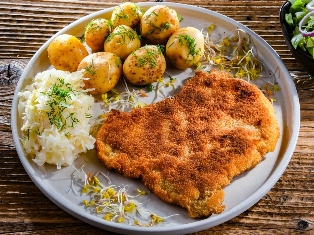 Schabowy smażony na smalcu, a na oleju roślinnym, podany z ziemniaczkami, surówką i kiełkami.