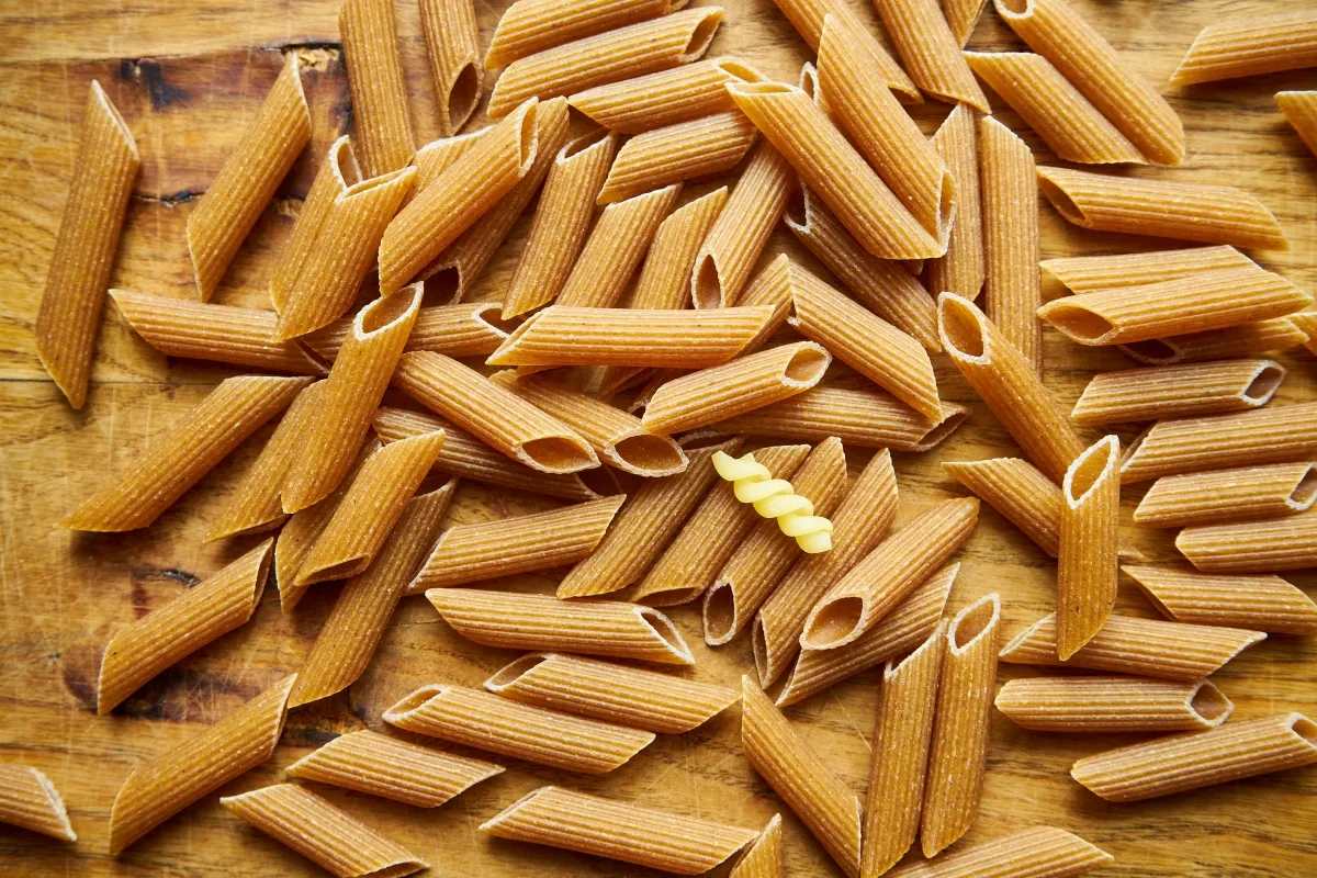 Makaron pełnoziarnisty vs zwykły: penne w odcieniach brązu i żółci, ułożone na drewnianym tle.