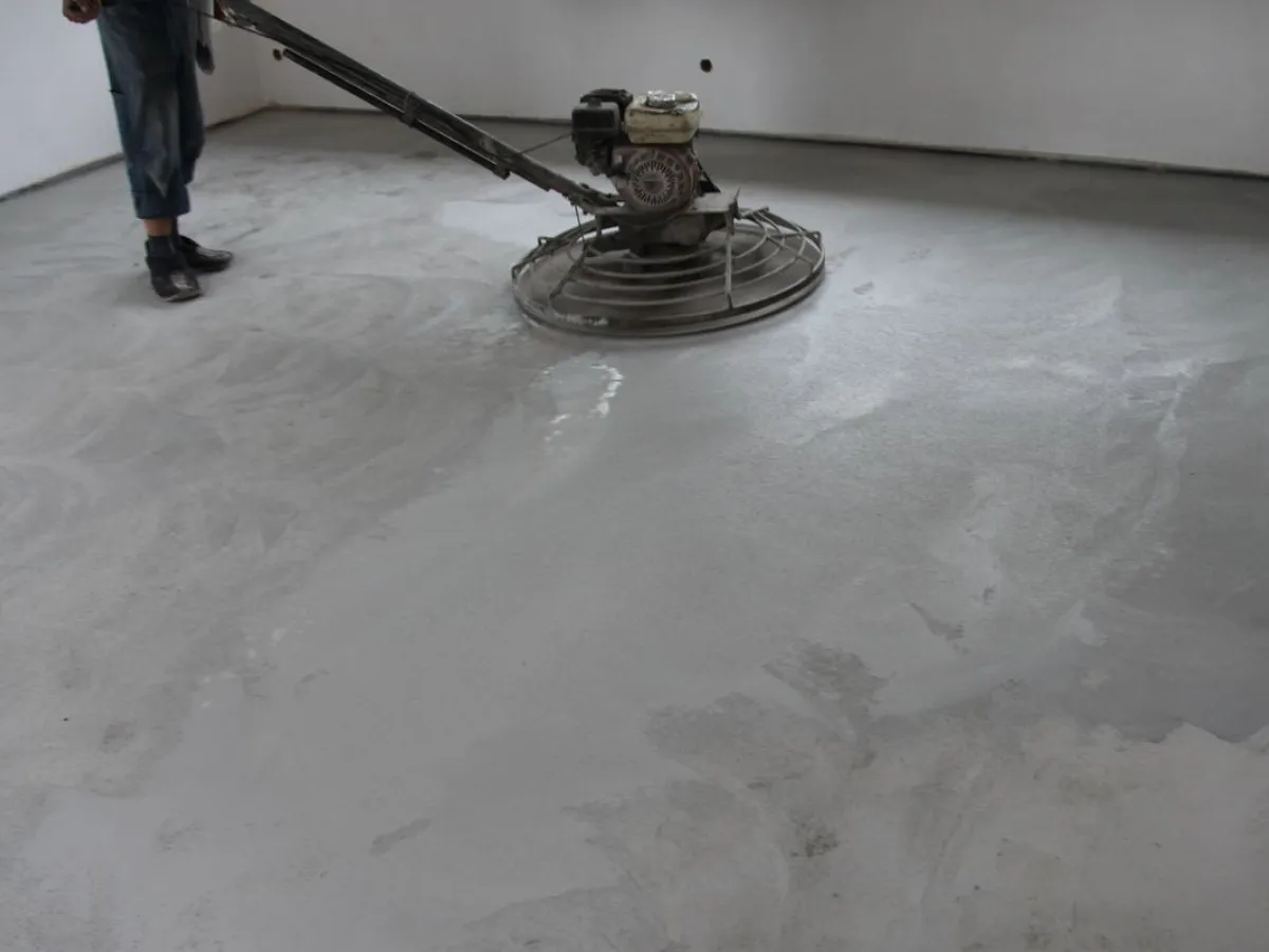 Pracownik wygładza świeżą wylewkę zacieraczką. Zastanawiasz się, ile cementu na 100m2 wylewki potrzeba?