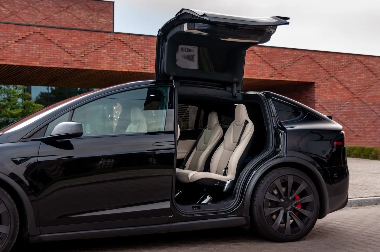 Czarna Tesla Model X z otwartymi drzwiami typu falcon wing i jasnymi sk&oacute;rzanymi fotelami. Zastanawiasz się, ile kosztuje najdroższa Tesla?